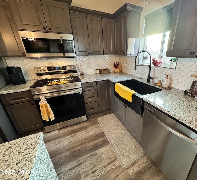 kitchen featuring a sink, light wood-type flooring, light stone countertops, and appliances with stainless steel finishes