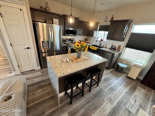 kitchen featuring dark brown cabinetry, decorative backsplash, wood finished floors, stainless steel appliances, and a sink