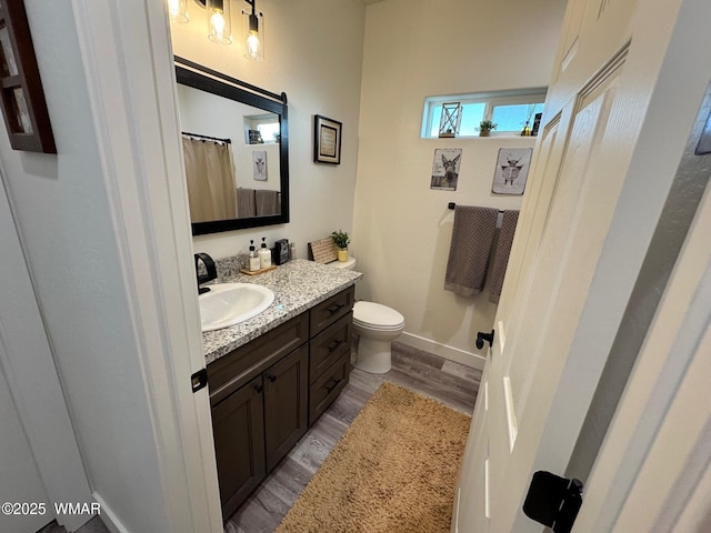 bathroom with toilet, vanity, baseboards, and wood finished floors