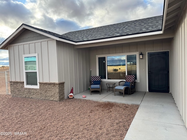 entrance to property with a patio area, board and batten siding, and a shingled roof