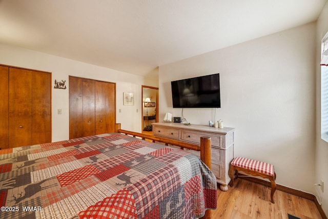 bedroom with light wood finished floors, baseboards, and multiple closets