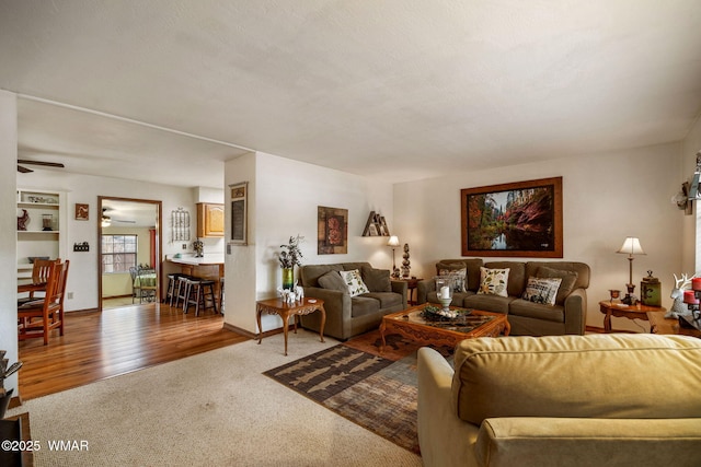 living room featuring a ceiling fan, baseboards, light carpet, and light wood finished floors