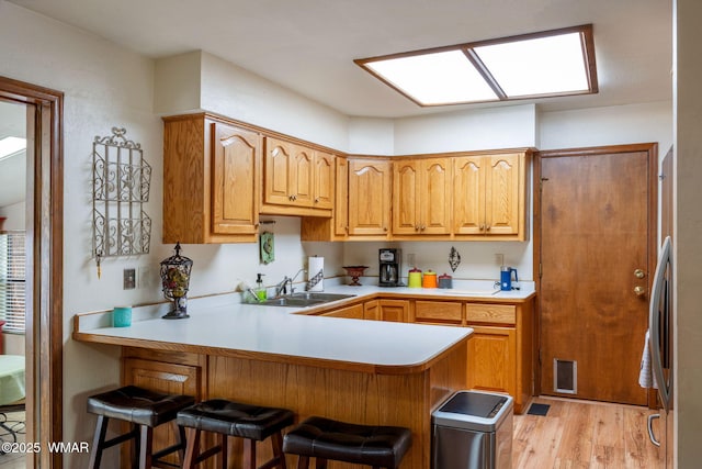 kitchen featuring a kitchen breakfast bar, a peninsula, light countertops, light wood-style floors, and a sink