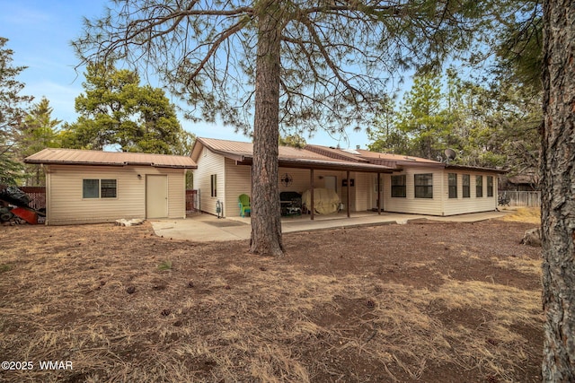 rear view of property with an outdoor structure, fence, metal roof, and a patio