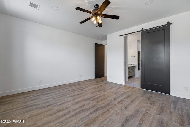 1738 W 7th St, Snowflake, AZ 85937 - unfurnished bedroom featuring a barn door, wood finished floors, baseboards, connected bathroom, and a ceiling fan