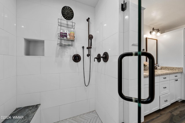 full bathroom with a tile shower, wood finished floors, and vanity