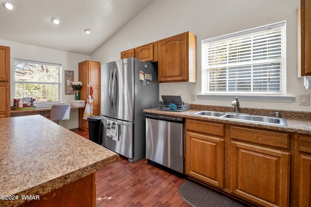 kitchen with brown cabinetry, dark wood-type flooring, vaulted ceiling, stainless steel appliances, and a sink