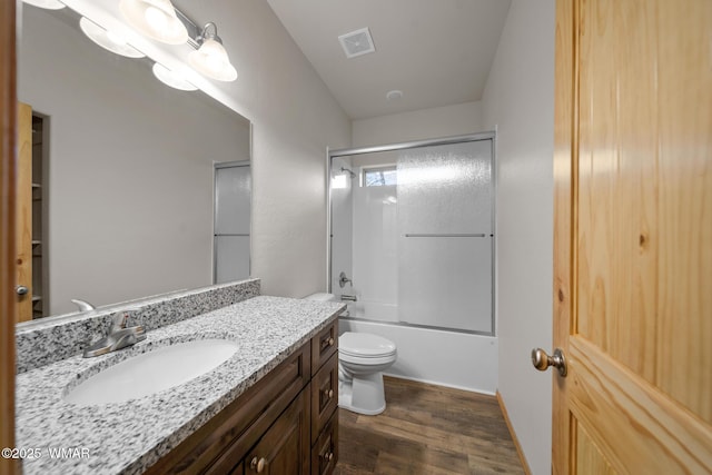 bathroom featuring visible vents, toilet, shower / bath combination with glass door, wood finished floors, and vanity