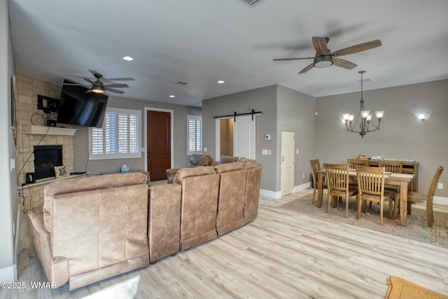 living area with a barn door, light wood-style flooring, ceiling fan with notable chandelier, a fireplace, and baseboards