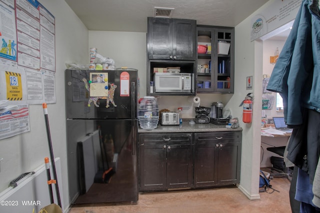 kitchen featuring visible vents, open shelves, white microwave, and freestanding refrigerator