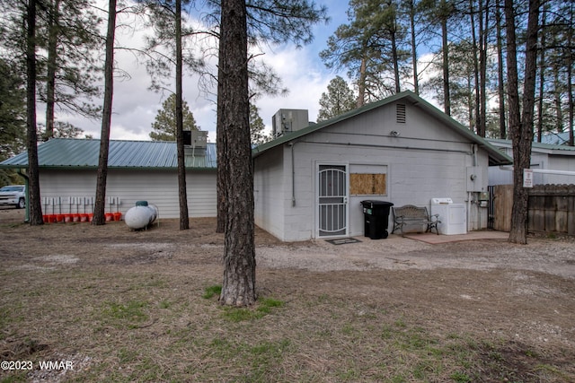 rear view of property featuring concrete block siding, fence, a chimney, and metal roof