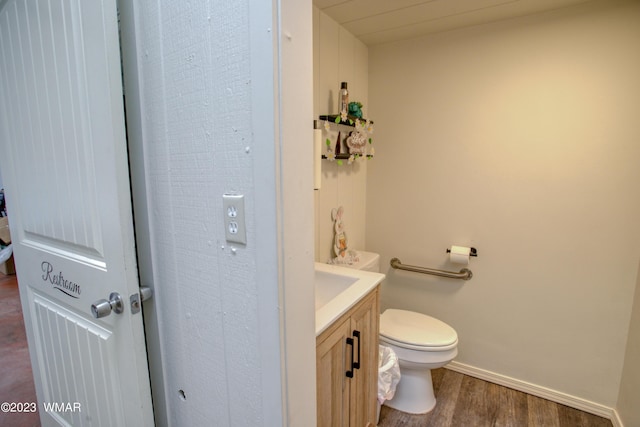 half bath featuring wood finished floors, vanity, toilet, and baseboards