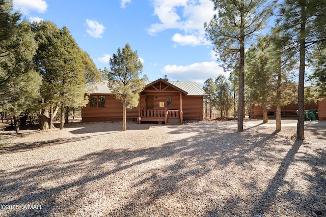 rear view of property featuring log veneer siding, metal roof, and a chimney