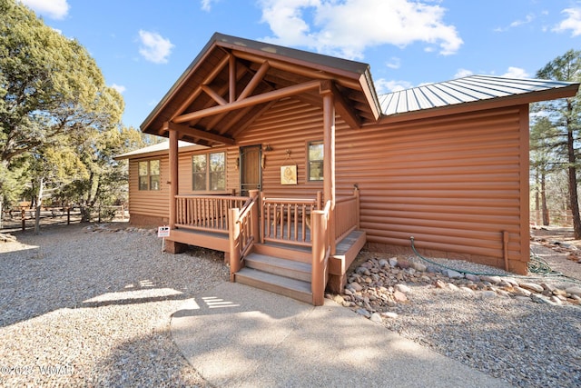 view of exterior entry featuring metal roof, log veneer siding, and fence