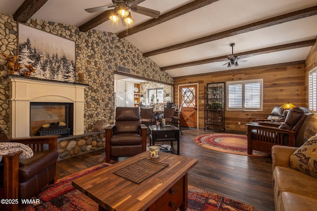 living room with vaulted ceiling with beams, visible vents, a ceiling fan, a glass covered fireplace, and dark wood-type flooring