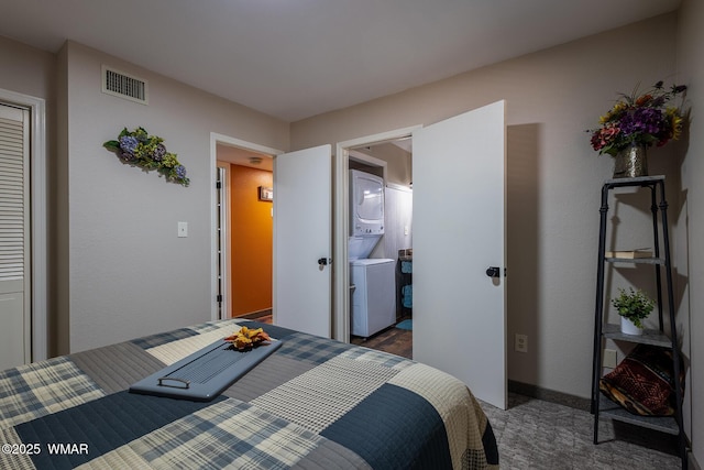 bedroom featuring baseboards, visible vents, ensuite bathroom, stacked washing maching and dryer, and dark carpet