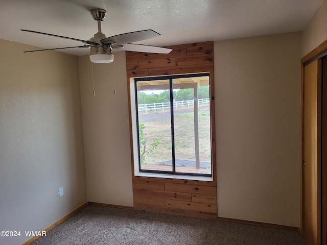 carpeted empty room with ceiling fan, a textured ceiling, baseboards, and wooden walls