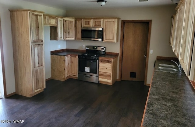 kitchen featuring dark wood-style flooring, dark countertops, appliances with stainless steel finishes, light brown cabinets, and a sink