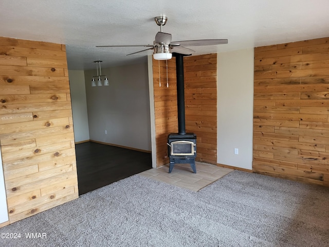 unfurnished living room featuring ceiling fan, a textured ceiling, a wood stove, and wooden walls