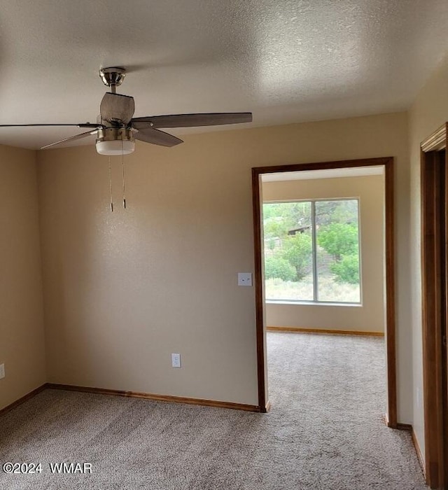 spare room featuring light carpet, a textured ceiling, a ceiling fan, and baseboards