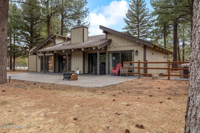 rear view of property featuring a shingled roof, a fire pit, a chimney, fence, and a patio area