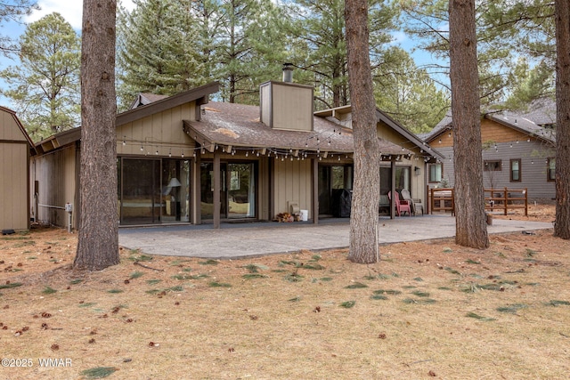 rear view of house with a patio, a shingled roof, a chimney, and board and batten siding