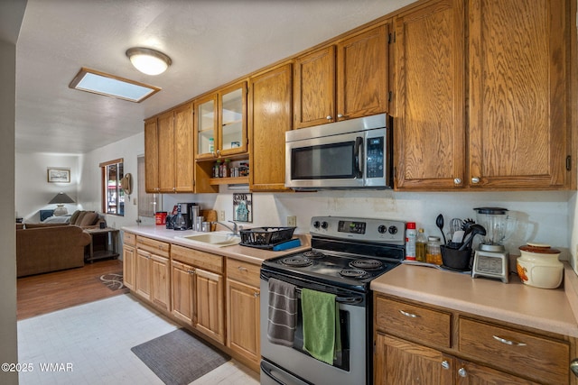 kitchen featuring stainless steel appliances, brown cabinetry, light countertops, and a sink