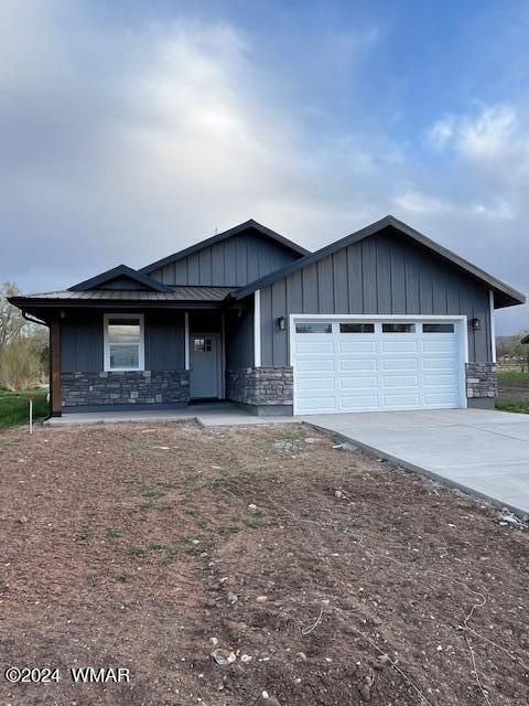 view of front facade with a porch, a garage, concrete driveway, stone siding, and board and batten siding