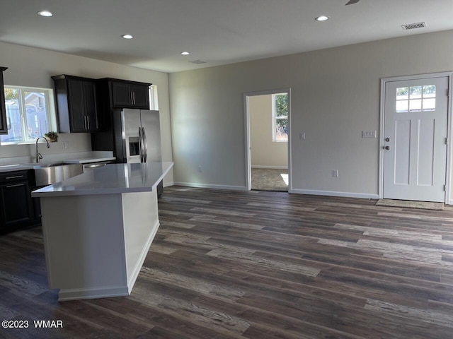 kitchen with visible vents, stainless steel fridge with ice dispenser, dark countertops, a center island, and a sink