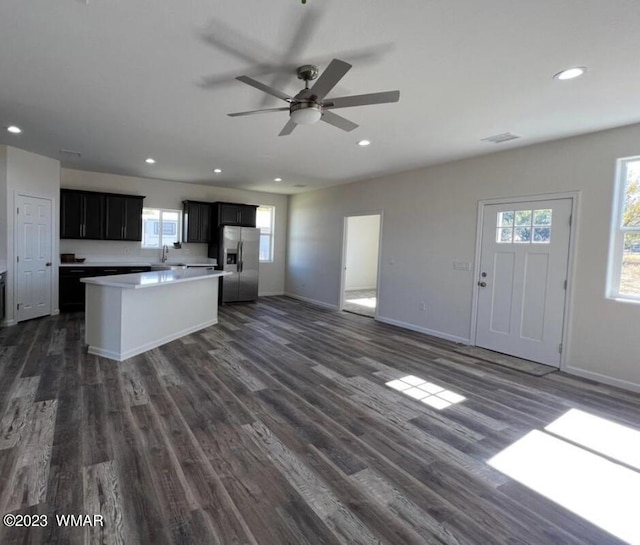 kitchen with a center island, stainless steel refrigerator with ice dispenser, light countertops, open floor plan, and dark cabinets