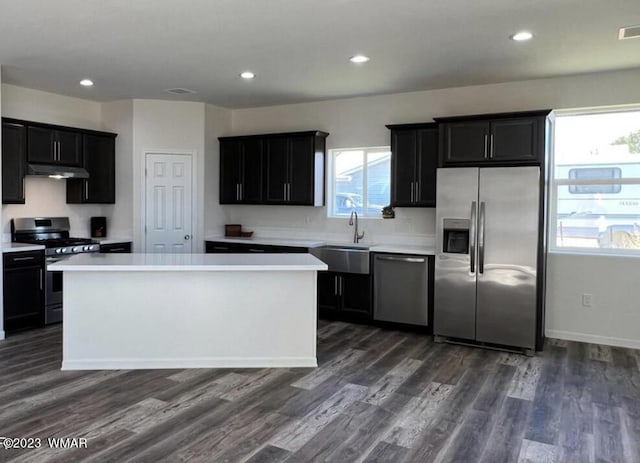 kitchen with stainless steel appliances, light countertops, a kitchen island, and dark cabinetry