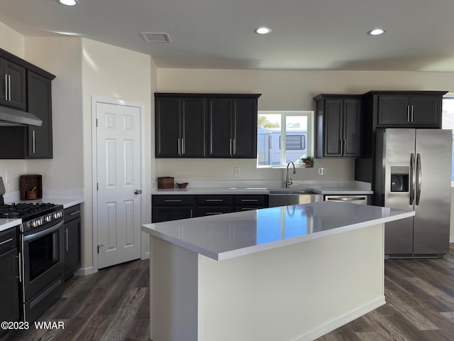 kitchen featuring a center island, dark wood-style flooring, light countertops, appliances with stainless steel finishes, and dark cabinetry