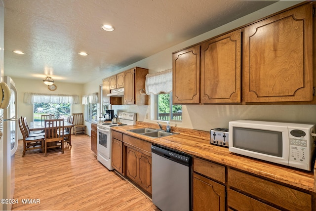 kitchen with brown cabinets, a sink, light wood-type flooring, white appliances, and under cabinet range hood