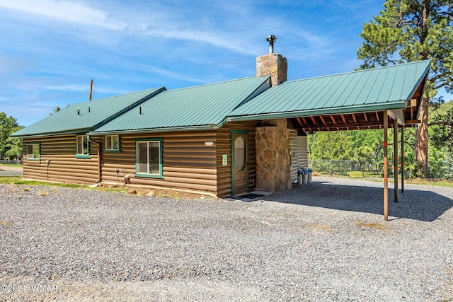 exterior space with driveway, a chimney, metal roof, and a carport