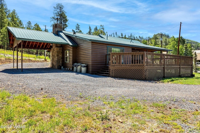 view of front of home with a chimney, metal roof, gravel driveway, a wooden deck, and a carport