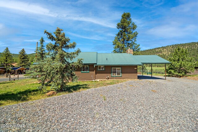 log home with gravel driveway, a chimney, metal roof, and a carport