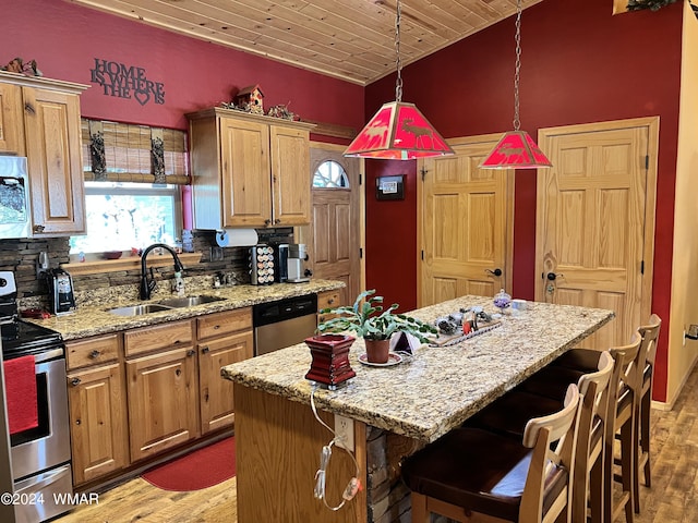 kitchen featuring light stone counters, decorative light fixtures, a center island, stainless steel appliances, and a sink