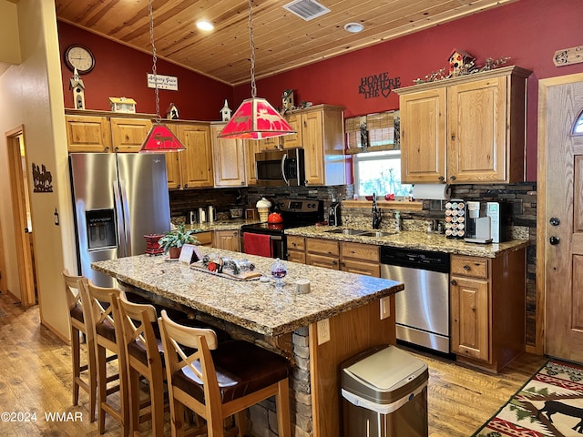 kitchen with a kitchen island, light stone counters, decorative light fixtures, stainless steel appliances, and a sink