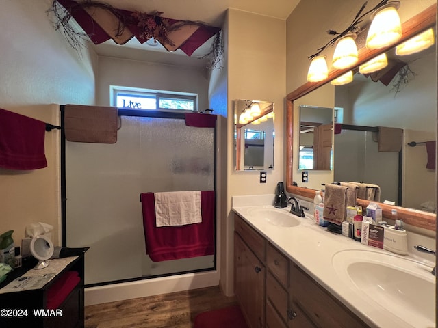 full bath with double vanity, a shower stall, a sink, and wood finished floors