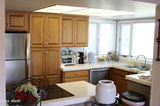 kitchen featuring brown cabinets, appliances with stainless steel finishes, a sink, and tile countertops