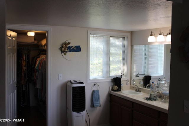 bathroom with a walk in closet, vanity, and a textured ceiling