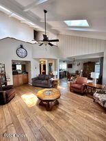 living room featuring a ceiling fan, beam ceiling, a towering ceiling, wood finished floors, and a skylight