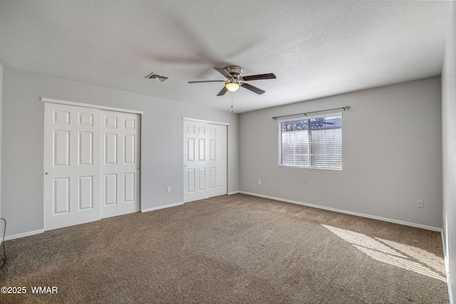 unfurnished bedroom with a textured ceiling, visible vents, baseboards, carpet, and two closets