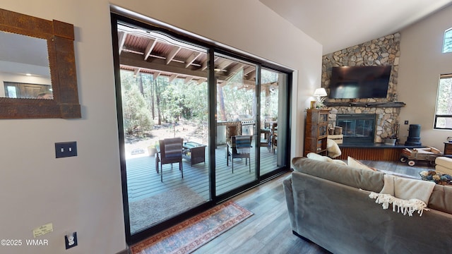 living room featuring a stone fireplace, wood finished floors, and lofted ceiling