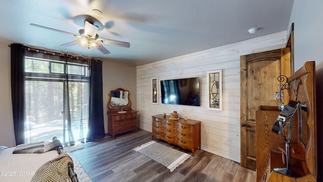 bedroom featuring a ceiling fan, wood walls, and wood finished floors