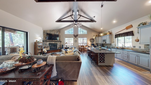 living area featuring ceiling fan, a stone fireplace, wood finished floors, lofted ceiling with beams, and recessed lighting
