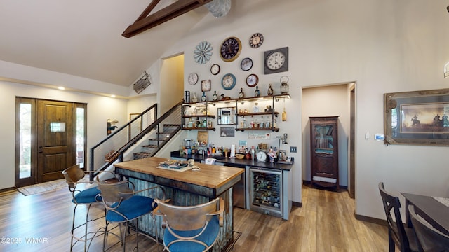 bar with a dry bar, wood finished floors, high vaulted ceiling, wine cooler, and stairs