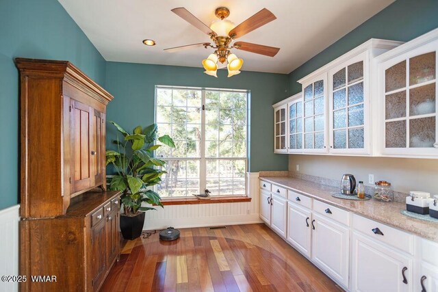 1961 S Canyon Ridge Trl, Show Low, AZ 85901 - kitchen featuring light wood finished floors, healthy amount of natural light, glass insert cabinets, a wainscoted wall, and a ceiling fan