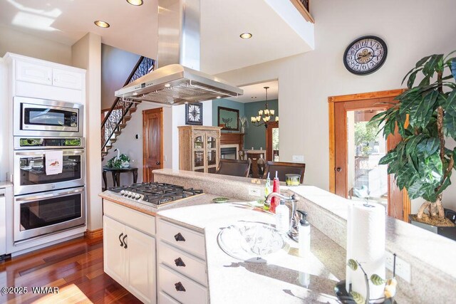 1961 S Canyon Ridge Trl, Show Low, AZ 85901 - kitchen with island exhaust hood, appliances with stainless steel finishes, light countertops, dark wood-style flooring, and a chandelier