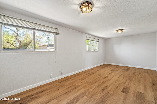 spare room featuring a textured ceiling, light wood-type flooring, and baseboards